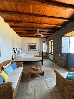A cozy room with a bed, wicker furniture, a ceiling fan, stone walls, and a stone floor. - Scalinata Tinos Sophisticated Living (Tinos)