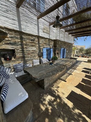A stone patio with outdoor seating, a stone wall, and a blue door. - Scalinata Tinos Sophisticated Living (Tinos)