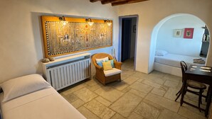 A cozy room with a bed, a wicker chair, a radiator, and a wall with a decorative panel. - Scalinata Tinos Sophisticated Living (Tinos)