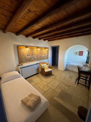 A cozy room with a bed, a wicker chair, a radiator, and a wall with a decorative panel. - Scalinata Tinos Sophisticated Living (Tinos)