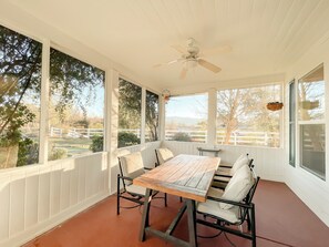 A covered patio with a table and chairs, large windows, and a ceiling fan. - Pickleball Retreat Near Bass Lake & S. Yosemite (Ahwahnee)