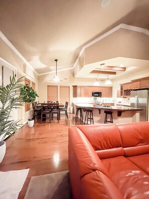 A modern kitchen with wooden cabinets, a dining area with a table and chairs, and a leather sofa in the foreground. - Pickleball Retreat Near Bass Lake & S. Yosemite (Ahwahnee)
