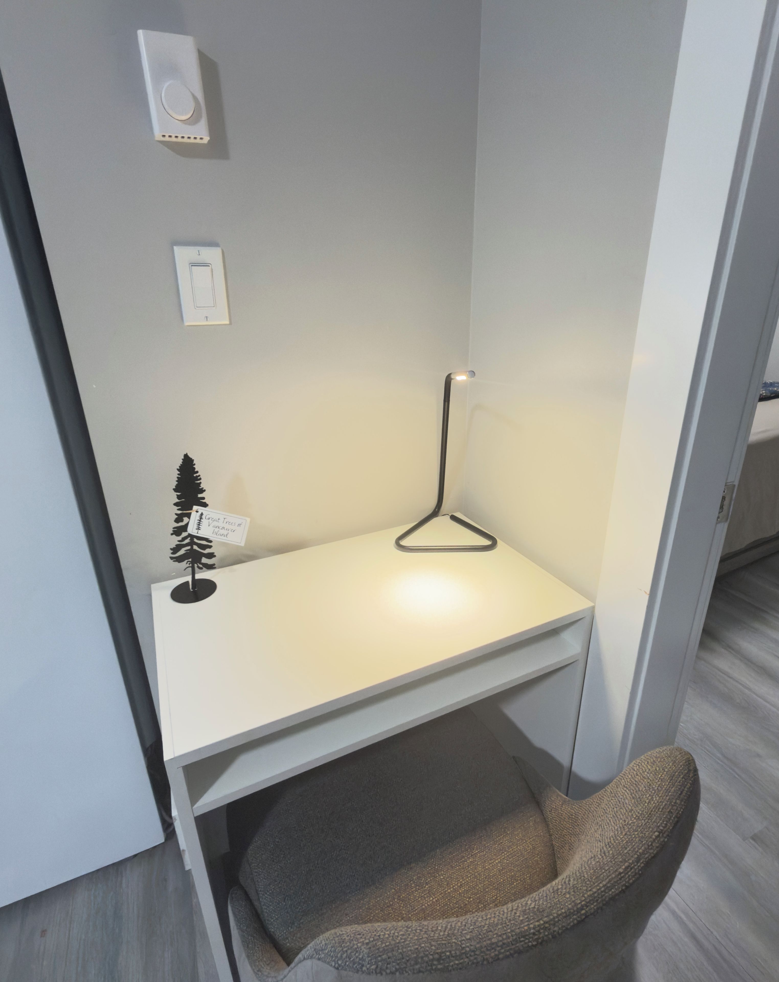 Un petit espace de travail clos, avec un bureau blanc, une lampe suspendue et une petite plante.