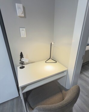 Et lille, lukket arbejdsrum med et hvidt skrivebord, en hængende lampe og en lille plante.