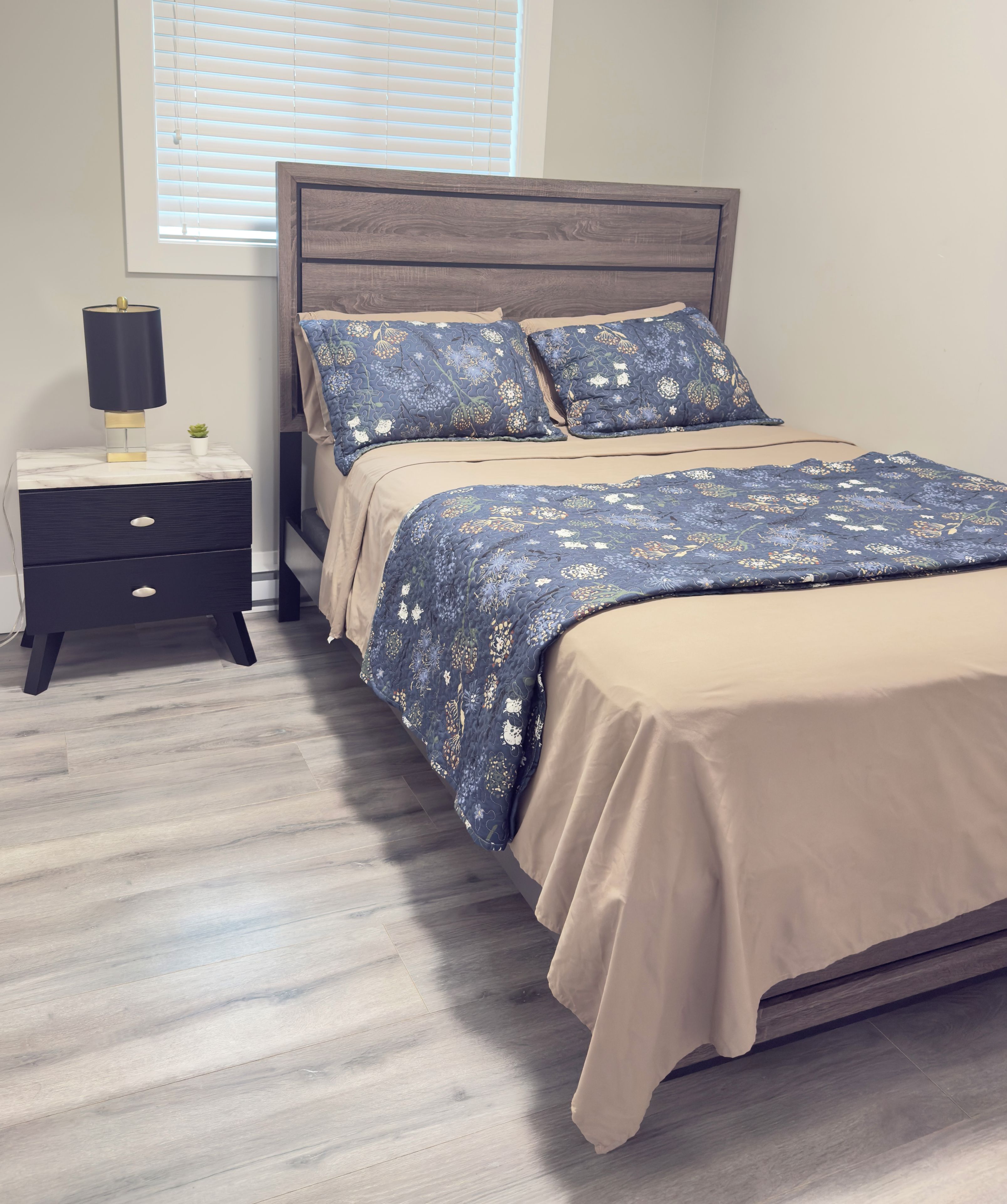 Une chambre à coucher avec un lit, une table de chevet, une lampe et une fenêtre avec des stores.