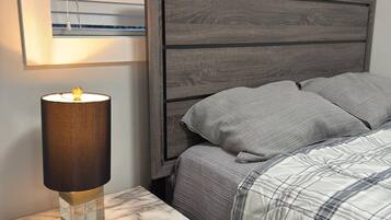A bedroom with a bed, a nightstand with a lamp, and a window with blinds.