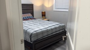 A bedroom with a bed, bedside table, lamp, and window with blinds. - Serene North Nanaimo suite close to Beaches, Woodgrove Mall and other amenities. (Nanaimo)