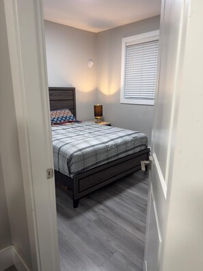Een slaapkamer met een bed, nachtkastje, lamp en raam met zonwering.