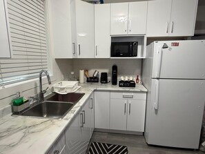 A compact kitchen with white cabinets, a built-in microwave, a refrigerator, and a sink with a faucet. - PORTSMOUTH COVE! Peaceful North Nanaimo Retreat. (Nanaimo)