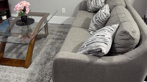 A living room with a grey sofa, a glass coffee table, and a potted plant. - Serene North Nanaimo suite close to Beaches, Woodgrove Mall and other amenities. (Nanaimo)