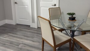 A dining area with a glass table and four chairs, two white doors, and a small potted plant on the wall. - Serene North Nanaimo suite close to Beaches, Woodgrove Mall and other amenities. (Nanaimo)