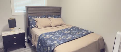 Un dormitorio con cama, mesita de noche, lámpara y ventana con persianas.