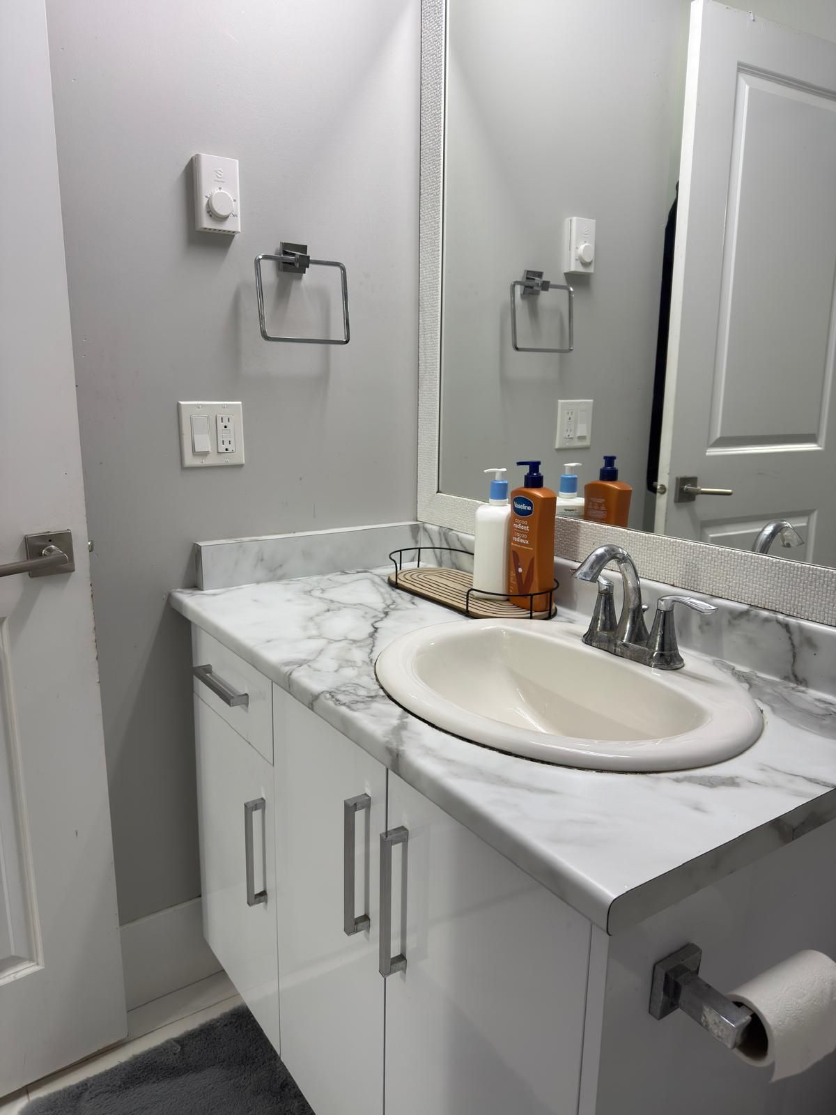 Een badkamer met een witte wastafel, een marmeren aanrechtblad en een spiegel erboven. Er staan toiletartikelen op het aanrechtblad en een handdoekhouder aan de muur.