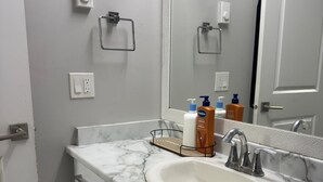 A bathroom with a white sink, marble countertop, and a mirror above it. There are toiletries on the countertop and a towel rack on the wall. - Serene North Nanaimo suite close to Beaches, Woodgrove Mall and other amenities. (Nanaimo)