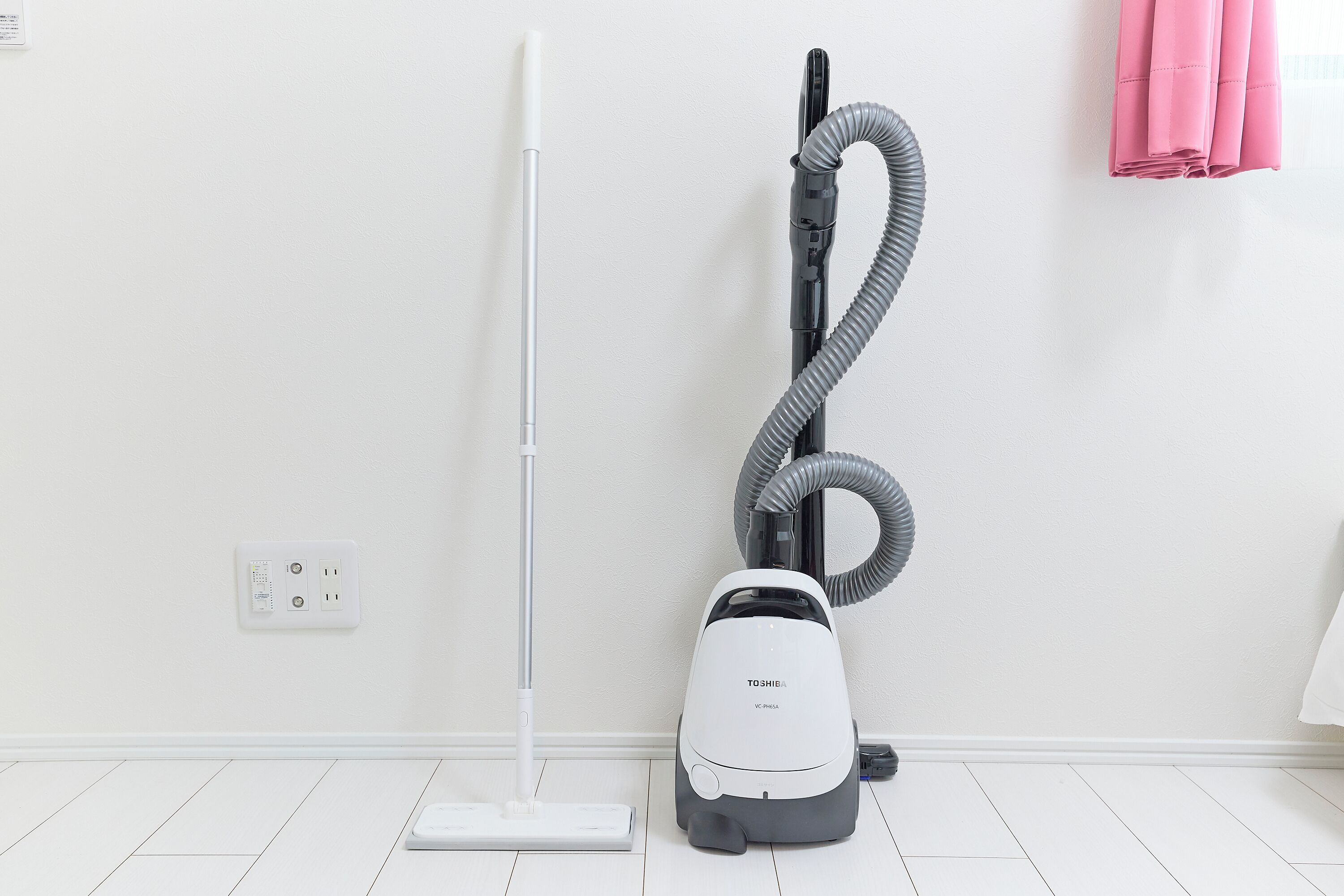 A vacuum cleaner and a mop in a room with white walls and a white floor.