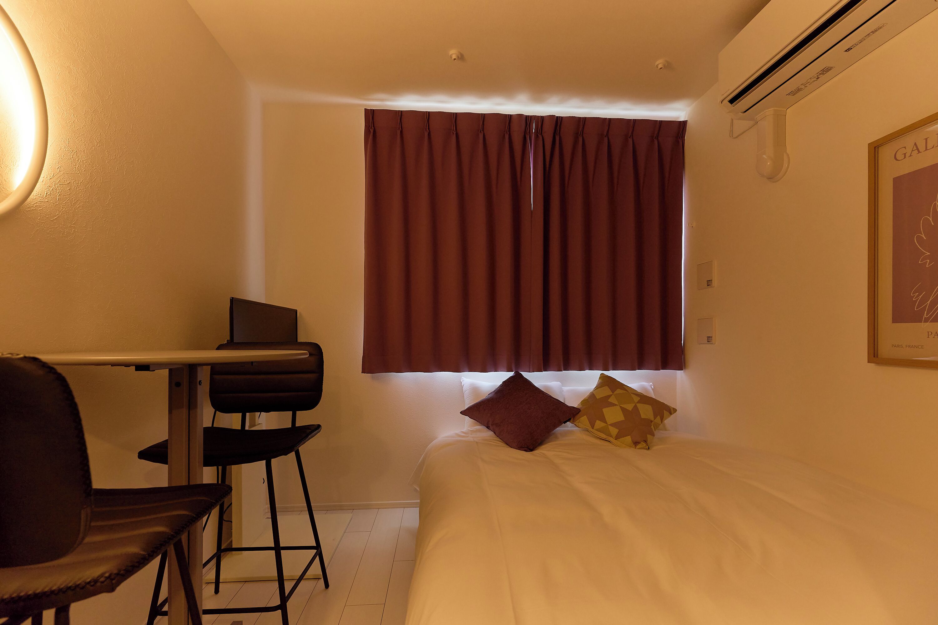 Ein Hotelzimmer mit Bett, Schreibtisch, Stuhl, einem Fenster mit Vorhängen und einer Klimaanlage.