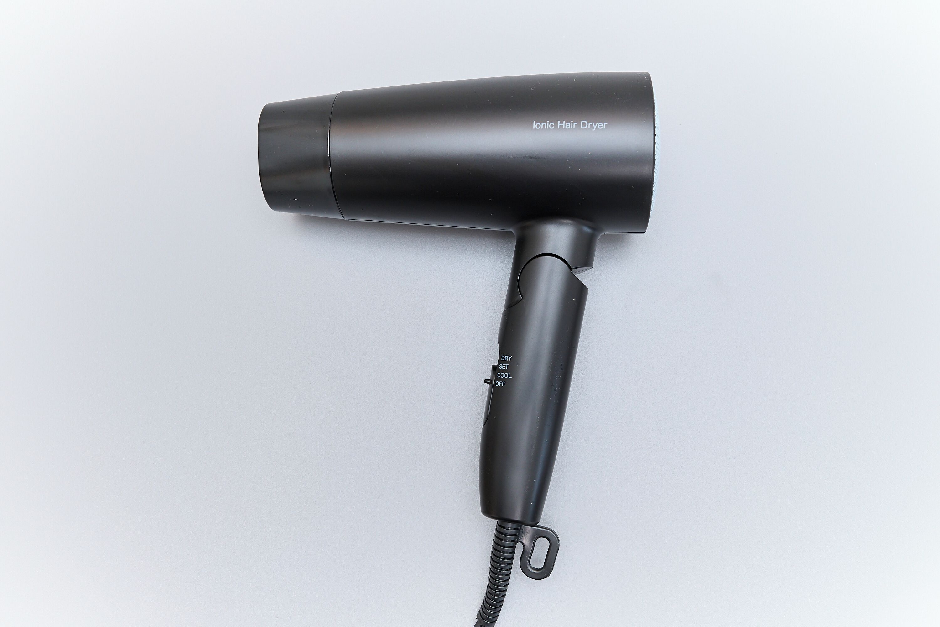 Un sèche-cheveux noir, muni d’un cordon et d’un interrupteur portant l’inscription « SÉCHAGE, AIR FROID ».