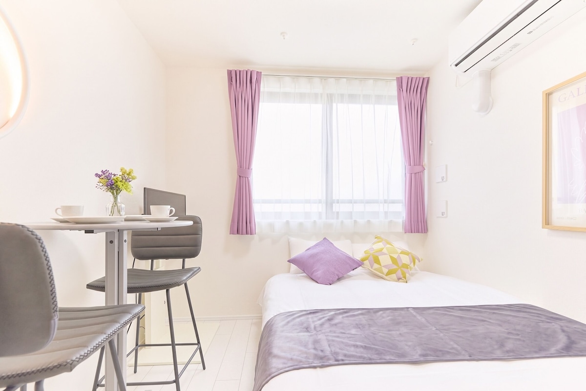 Una habitació d'hotel amb un llit, un escriptori amb una cadira, una finestra amb cortines i un aire condicionat fixat a la paret.