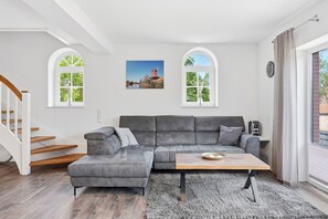 Ein modernes Wohnzimmer mit einem grauen Ecksofa, einem Holztisch und einer Treppe.
