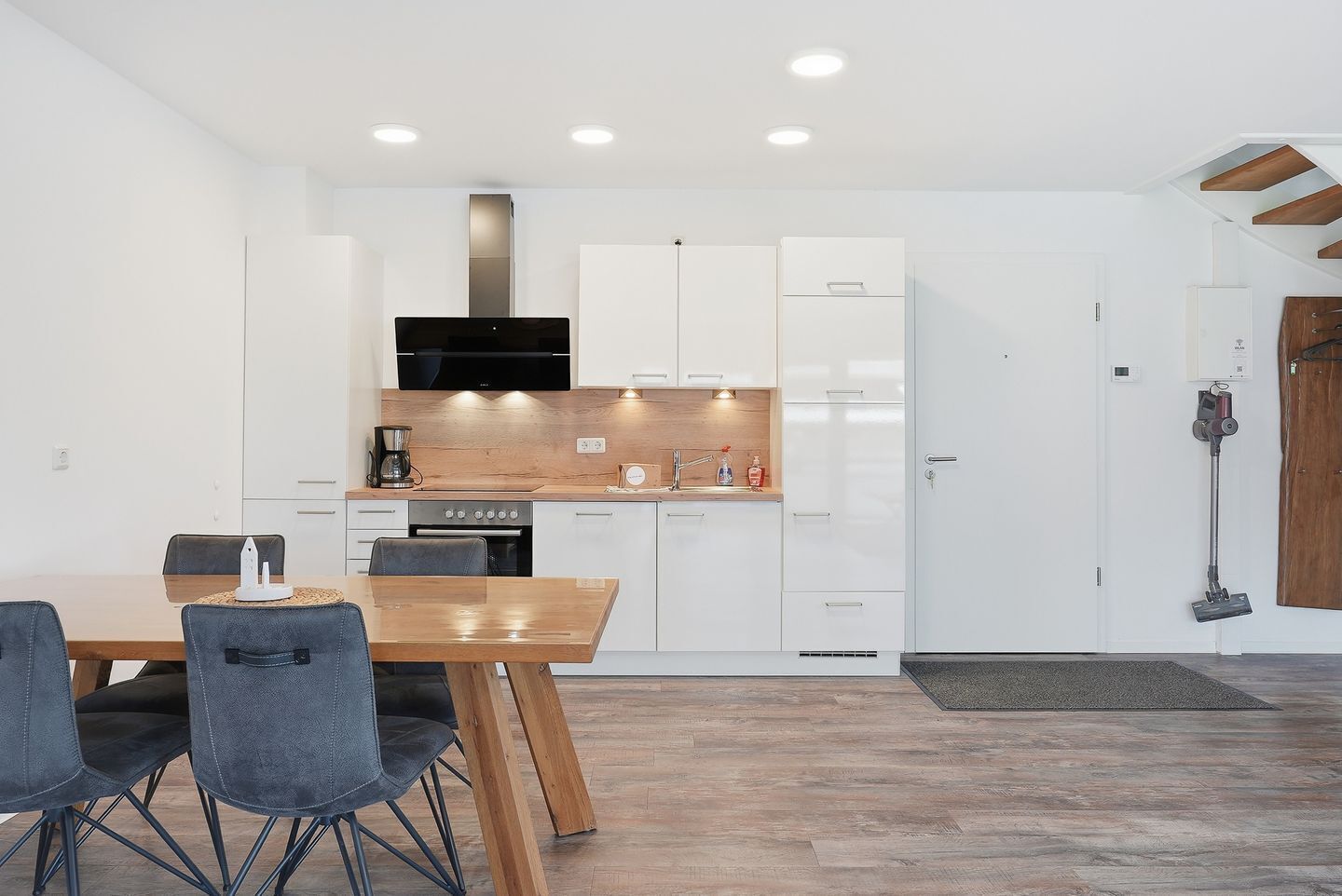 A modern kitchen with white cabinetry, a wooden dining table, and a built-in oven.