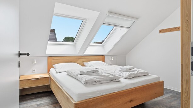 A bedroom with a sloped ceiling, skylights, a wooden bed frame, and a nightstand. - To the Anchorage - To the Anchorage: Vacation near Greetsiel with a large terrace (Krummhörn)