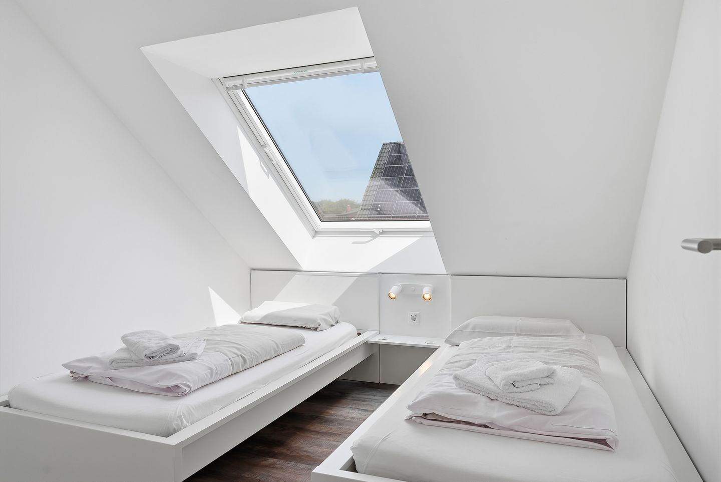Un dormitorio moderno con dos camas, un tragaluz y vistas a un edificio.