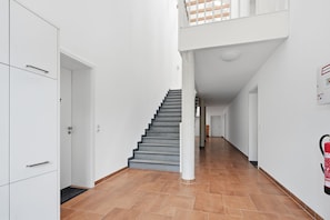 Ein modernes Interieur mit einer Treppe, die zu einer zweiten Etage führt, weißen Wänden und einem an der Wand befestigten Feuerlöscher.