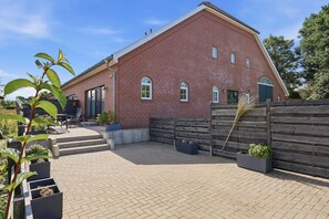 A red brick building with a sloped roof, a wooden fence, and a paved patio area with planters. - To the Anchorage - To the Anchorage: Vacation near Greetsiel with a large terrace (Krummhörn)