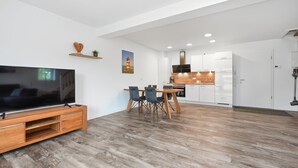 A modern living room with a flat-screen TV, wooden entertainment unit, and a dining area with a table and chairs. - To the Anchorage - To the Anchorage: Vacation near Greetsiel with a large terrace (Krummhörn)