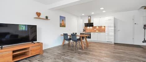 A modern living room with a flat-screen TV, wooden entertainment unit, and a dining area with a table and chairs.