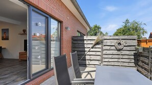 A patio with a table and chairs, a wooden fence, and a glass door leading to a room with a view. - To the Little Lighthouse - To the Little Lighthouse: A Vacation in Idyllic Pilsum (Krummhörn)