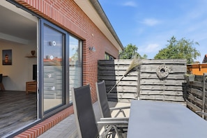 Eine Terrasse mit Tisch und Stühlen, ein Holzzaun und eine Glastür, die zu einem Raum mit Blick führt.