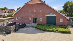 A red brick building with a steeply pitched roof, a green door, and a small set of stairs leading to the entrance. - To the Little Lighthouse - To the Little Lighthouse: A Vacation in Idyllic Pilsum (Krummhörn)