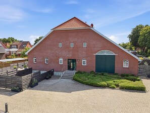 Ein Gebäude aus roten Ziegeln mit einem steilen Satteldach, einer grünen Tür und einer kleinen Treppe, die zum Eingang führt.