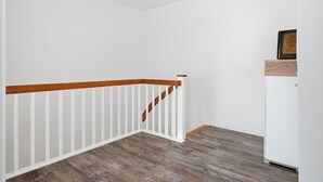 A corner of a room with a wooden staircase railing, a white wall, and a white cabinet. - To the Little Lighthouse - To the Little Lighthouse: A Vacation in Idyllic Pilsum (Krummhörn)