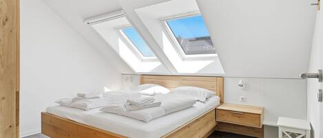 A bedroom with a skylight, wooden bed, bedside table, and a small white stool.