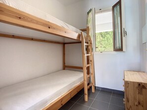 Ein Etagenbett mit Holzleiter, ein Fenster mit Vorhängen und ein kleines Holzschränkchen.