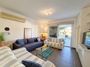Ein Wohnzimmer mit einer Couch, einem Sofas mit Muster, einem Couchtisch, einem Fernseher und einer Glastür, die zu einem Außenbereich führt.