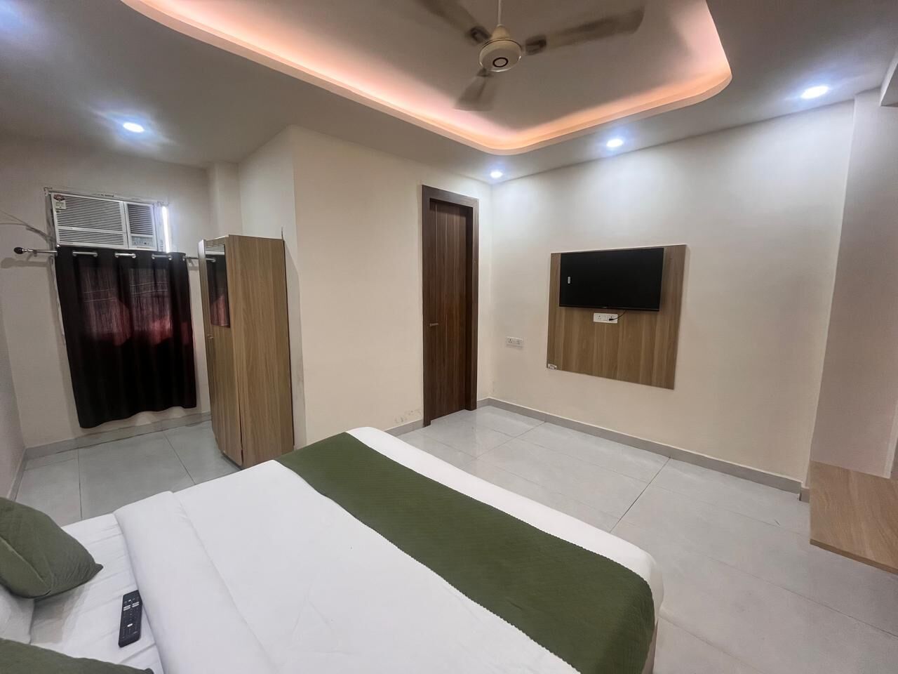 Una habitación de hotel con cama, armario, televisor montado en la pared y aire acondicionado.