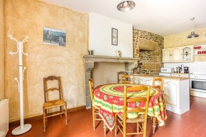 Eine Küche mit Steinwand, Kamin, Esstisch mit Stühlen und einem Garderobenhaken.