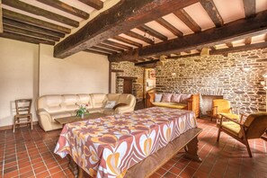 Ein rustikales Interieur mit Steinwänden, Holzbalkendecke, einer Couch, einem Tisch und einem Stuhl.