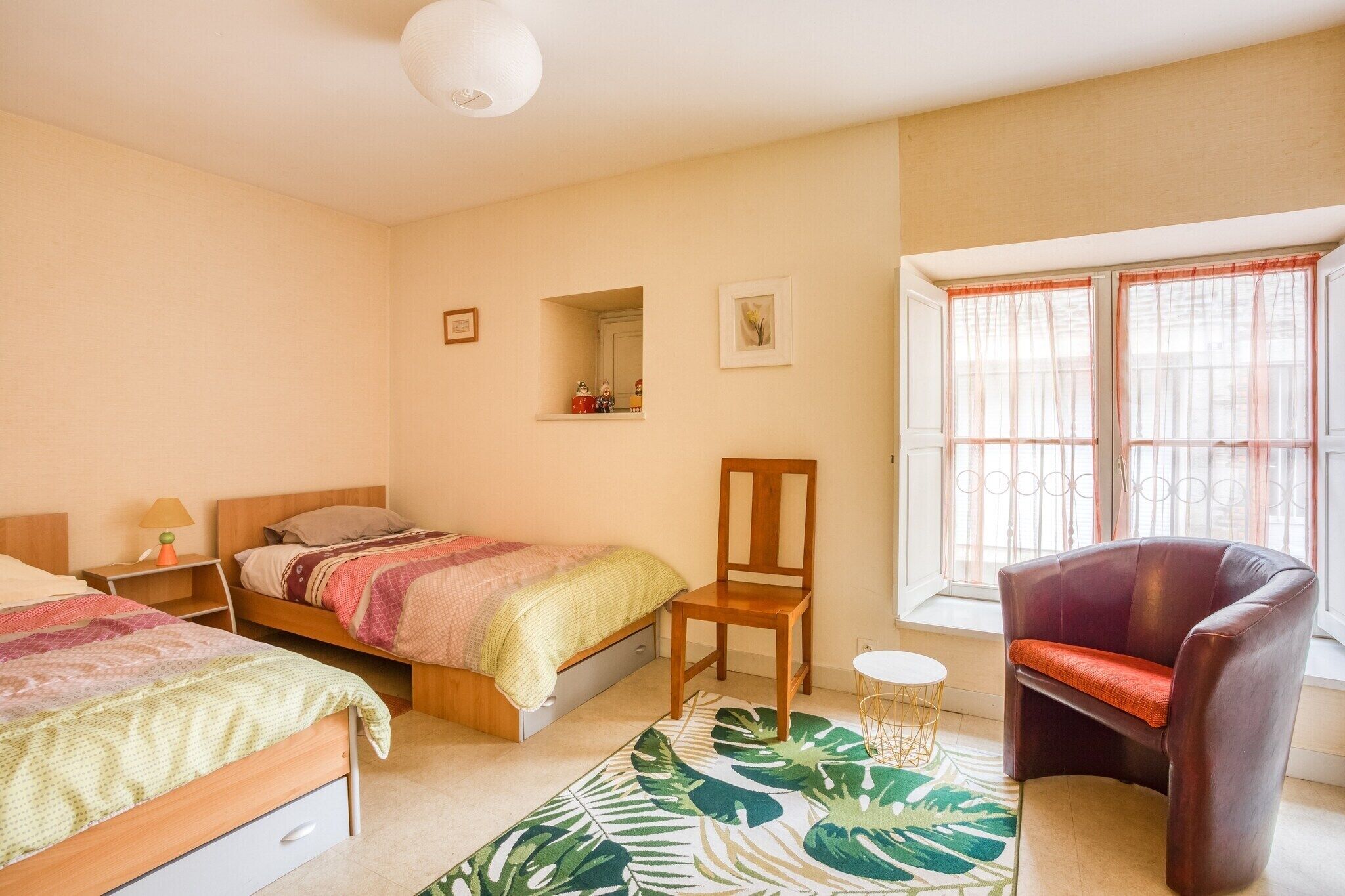 A bedroom with two beds, a chair, a small table, and a window with curtains.