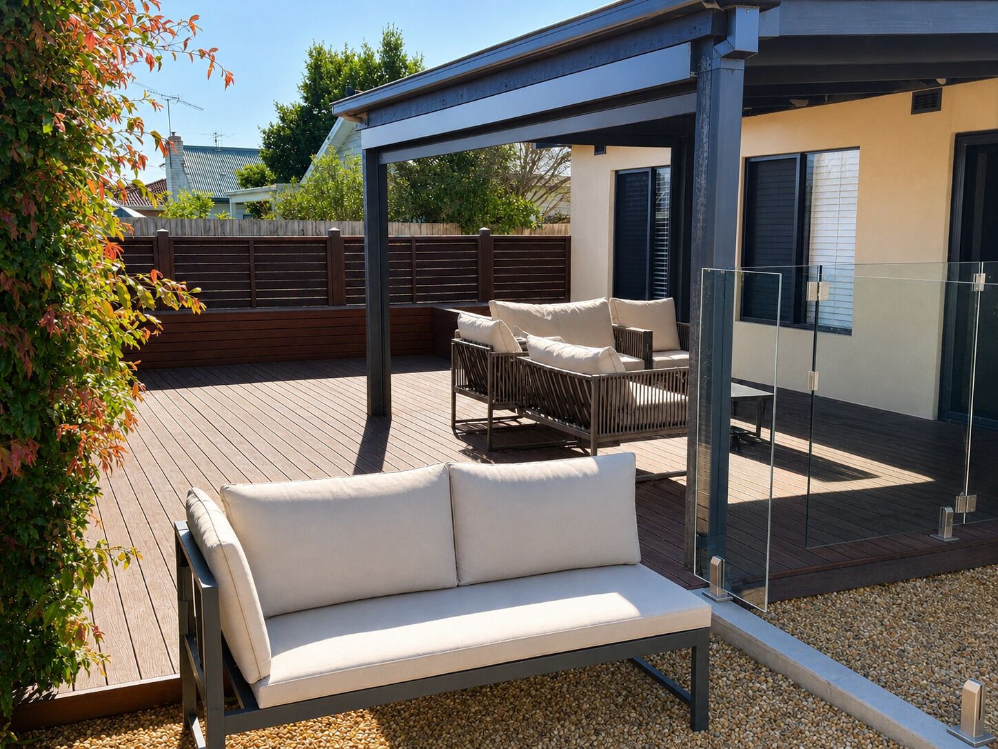 An outdoor patio with a cushioned sofa, a glass enclosure, and a wooden deck.