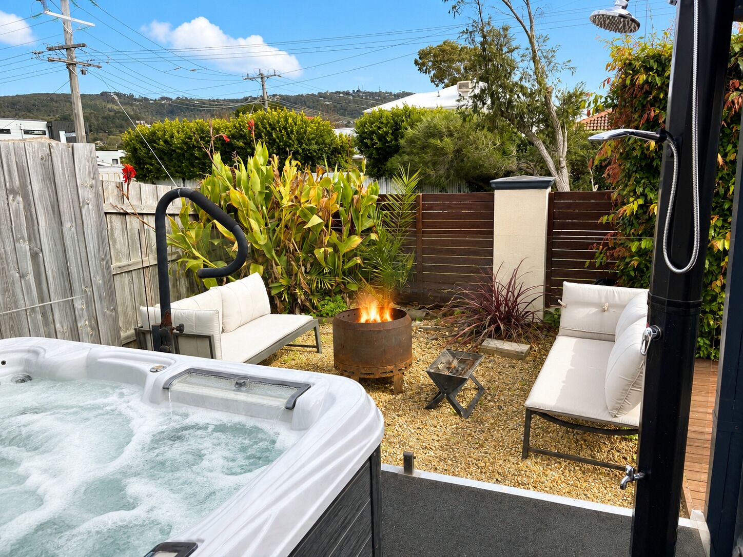 A hot tub with a fire feature, surrounded by outdoor furniture and a garden.