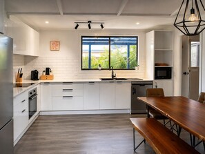 Una cocina moderna con armarios blancos, una mesa de comedor de madera y un amplio ventanal con vistas a zonas verdes.