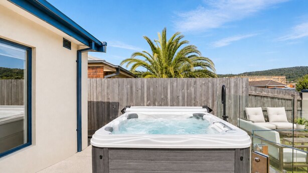 Ein Whirlpool in einem Garten mit Holzzaun, einer Palme und blauem Himmel.