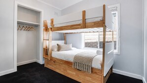 Ein Stockbett mit Holzrahmen, ein Kleiderschrank mit Ablagefläche und ein Fenster mit Blick auf Gebäude.