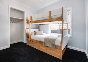 Ein Stockbett mit Holzrahmen, ein Kleiderschrank mit Ablagefläche und ein Fenster mit Blick auf Gebäude.