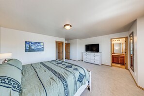 Un dormitorio con cama, cómoda, televisor, un cuadro y una puerta que da a otra habitación.