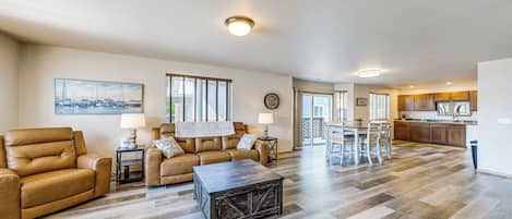 A spacious living room with a sofa, coffee table, and dining area, leading to a kitchen with wooden flooring.
